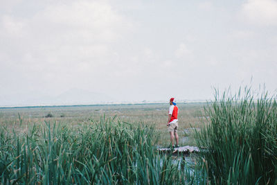 Rear view of man standing on grassy field against cloudy sky