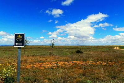 Road sign on field against sky
