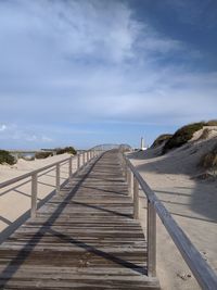 Boardwalk leading towards pier at beach against sky