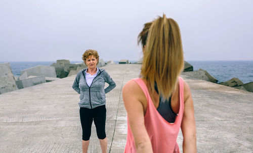 Woman with mother exercising on pier against sky
