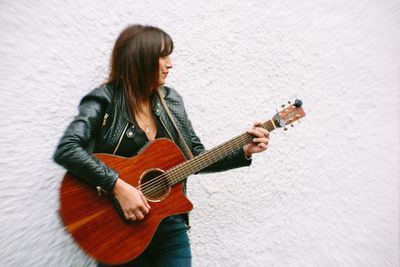 Mature woman playing guitar against white wall