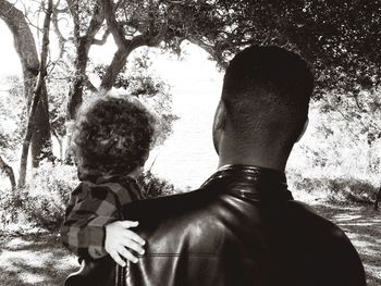 Rear view of father with son standing against trees