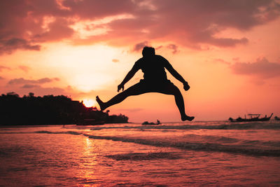 Silhouette man jumping in sea against sky during sunset