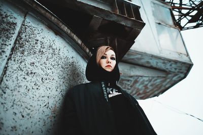 Portrait of young woman standing against building