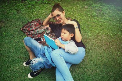 High angle view of mother and son using digital tablet while lying on field