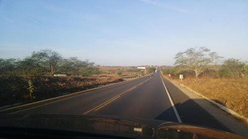 Road amidst trees against clear sky seen through car windshield