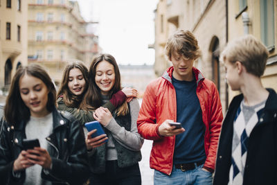 Male and female friends using smart phone in city