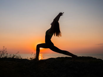 Side view of woman doing exercising on field against sea during sunset
