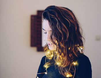 Close-up of young woman with illuminated string lights at home