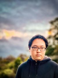 Portrait of young man in eyeglasses against cloudy sunset sky.