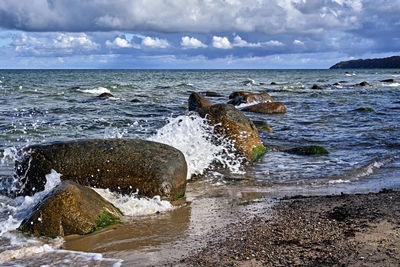 Sea waves splashing on rocks against sky