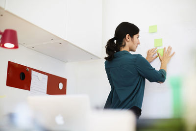 Rear view of mid adult businesswoman placing sticky notes on whiteboard in office