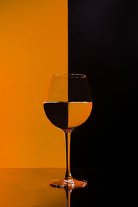 Close-up of wineglass on table against orange background