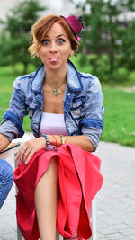 Portrait of young woman sticking out tongue while sitting on stool