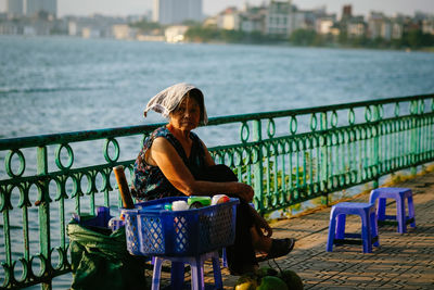 Portrait of woman sitting on bench against lake