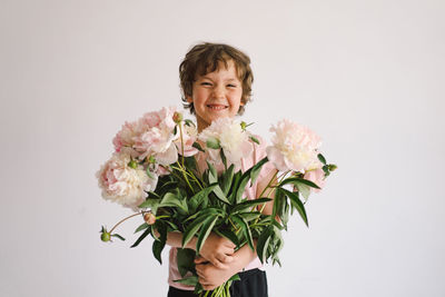 Cheerful happy child with peonys bouquet. smiling little boy on white background.