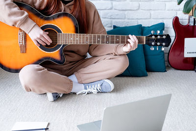 Midsection of man playing guitar on sofa at home