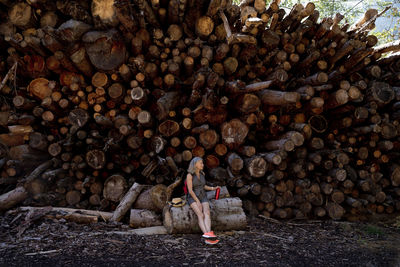 Senior woman sitting on log in front of stack of wood