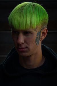 Close-up of man with dyed hair standing against black background
