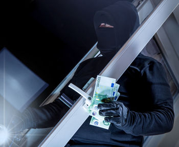 Close-up of robber with paper currency standing outdoors at night