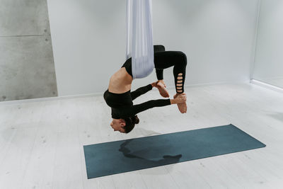 Full length of ballet dancer hanging on textile at gym