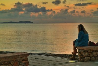 Woman sitting on beach at sunset