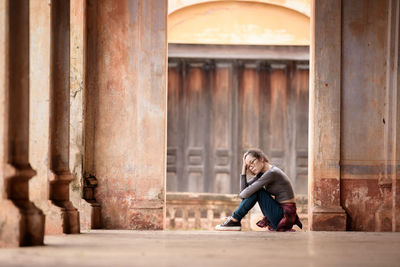Full length portrait of man sitting on building