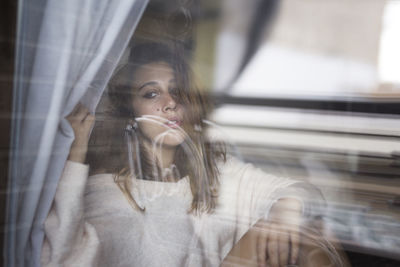 Portrait of young woman looking through window