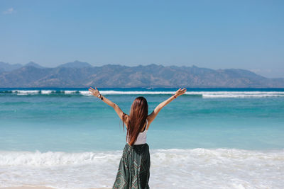 Rear view of young woman standing at beach against sky