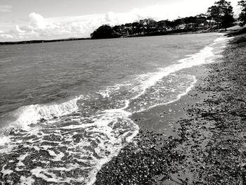 Waves rushing towards shore against sky