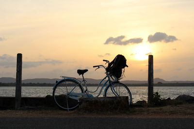 Bicycle on beach against sky during sunset