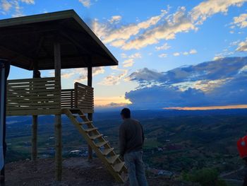 Rear view of man standing at shore against sky during sunset