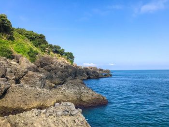 Rocks by sea against blue sky