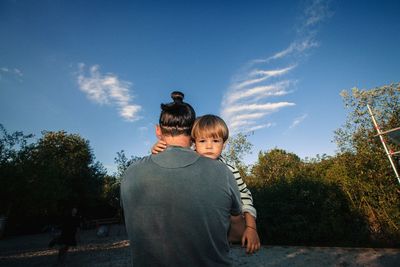 Rear view of father carrying son on field against sky