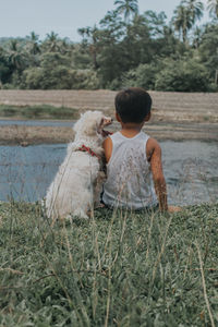 Rear view of boy with dog sitting on land