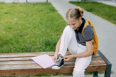 A cute teenage girl is sitting on a bench and tying her shoelaces