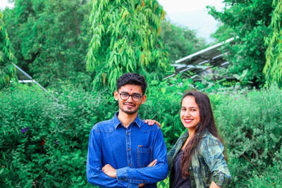 Portrait of smiling young couple standing against trees in forest