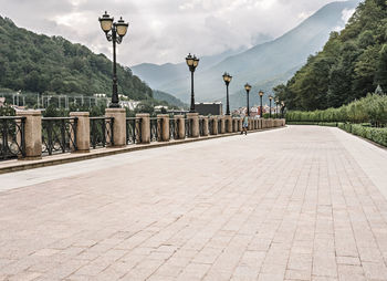 Young man in distance riding on roller skates along embankment against background wooded mountains 