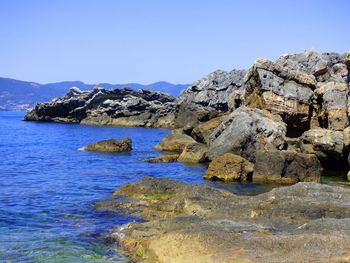 Rock formations by sea against clear blue sky