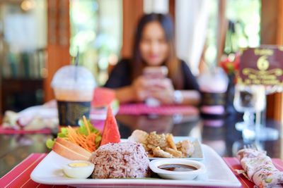 Close-up of food in plate on table with woman sitting in background at restaurant