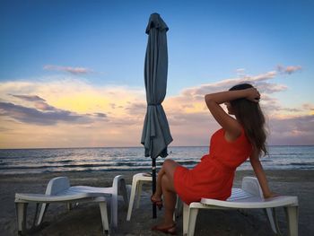 Woman in orange dress sittting on a sunbed and looking at the ocean