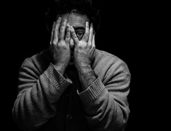 Portrait of man with hands covering face against black background