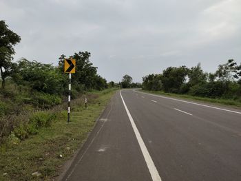 Road sign by trees against sky