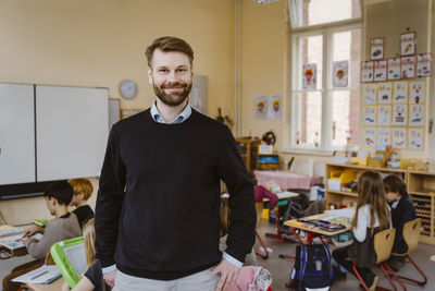 Portrait of smiling bearded teacher standing in front of students at classroom