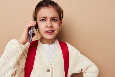 Portrait of girl talking on phone against beige background
