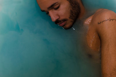 Shirtless young man with eyes closed while standing in swimming pool