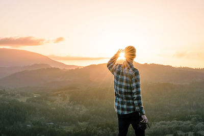 Rear view of man looking at view while standing on mountain against sky during sunset