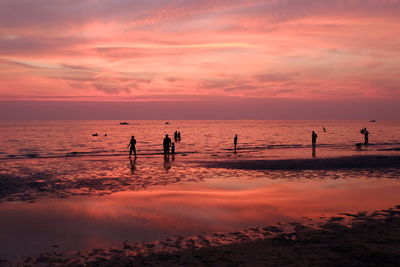 Silhouette people on beach against sky during sunset