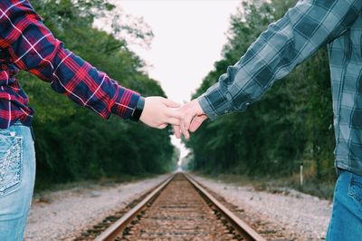 Midsection of couple with holding hands over railroad track against trees