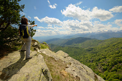 Man standing on rock looking at mountains against sky